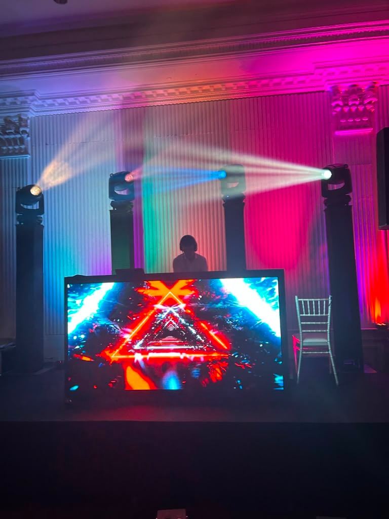 LED DJ booth with moving-head beams in a pink and purple uplit hall